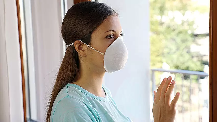 Frau mit Atemmaske steht am Fenster